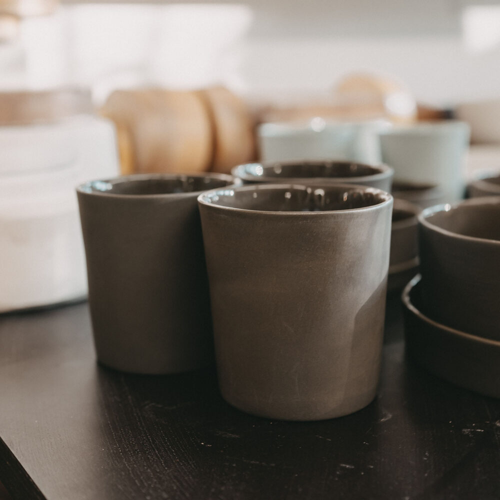 Porzellan Tassen in braun auf schwarzer Oberfläche und weiterem Keramik-Geschirr als unscharfer Hintergrund