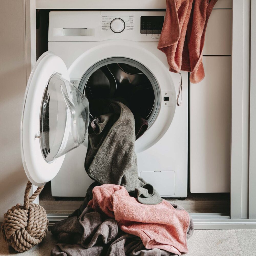 Waschmaschine mit davorliegender Wäsche in beiger Umgebung und Seilspielzeug für Hunde