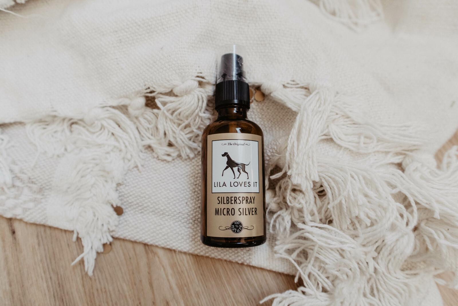 Braune Sprühflasche Desinfektionsspray für Hunde mit Silber auf einem weißen Teppich und hell-braunem Holzboden | LILA LOVES IT "Silberspray für Hunde"