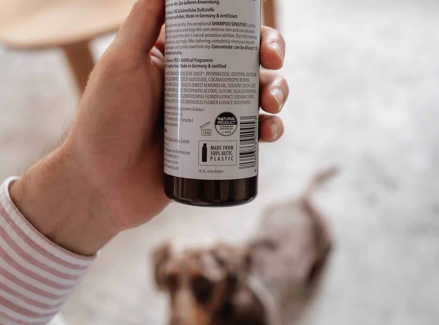 Rückseite einer LILA LOVES IT Shampoo Flasche mit Hand und Hund im Hintergrund